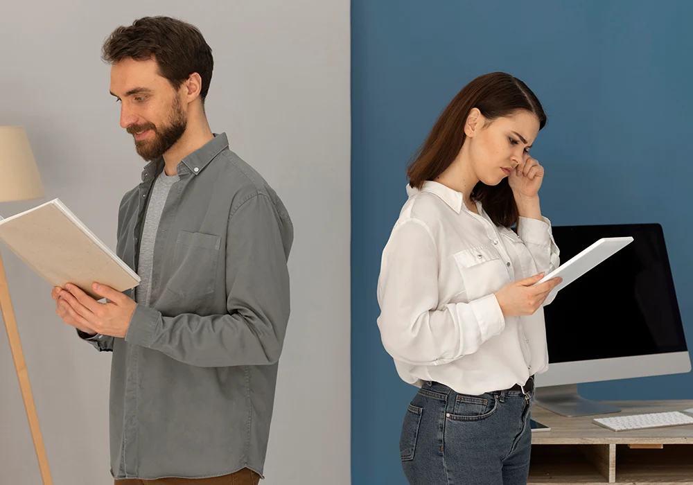 Hombre leyendo un cuaderno mientras sonríe y mujer mirando su tablet, pensativa, en un entorno de oficina moderna con escritorios y una computadora.